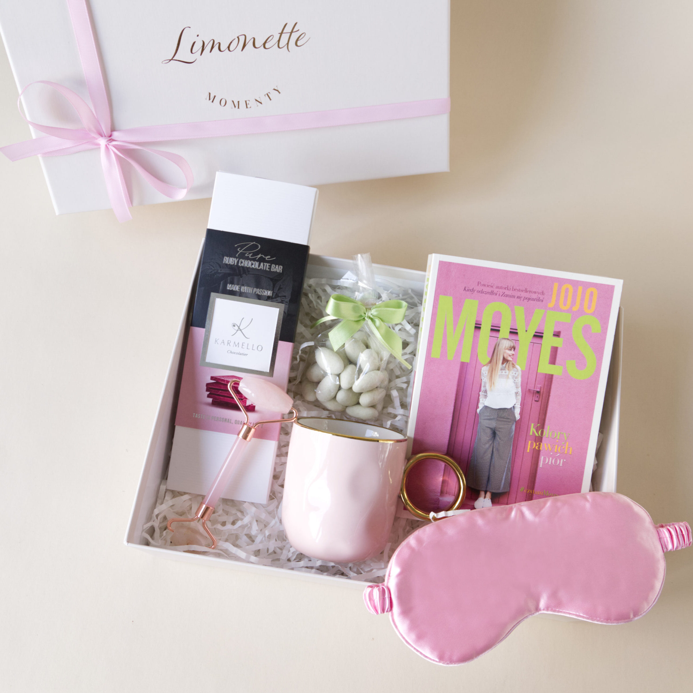 Przyjemności w Różowych Odcieniach 3 Zestaw prezentowy zawiera: Książka Kolory Pawich Piór, Opaska na oczy, różowy kubek, migdały w czekoladzie, czekolada ruby, roller do twarzy.